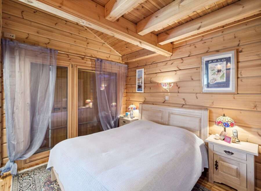 Experience rustic charm in this cozy log cabin bedroom, featuring a comfortable bed adorned with a white knit blanket.