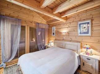 Experience rustic charm in this cozy log cabin bedroom, featuring a comfortable bed adorned with a white knit blanket.