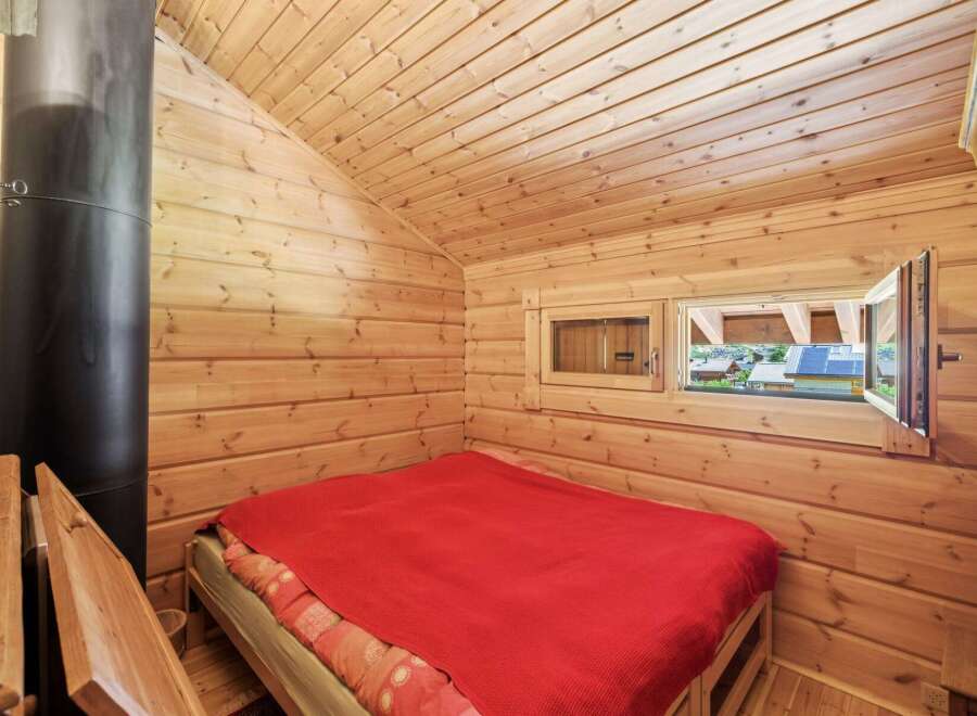 Experience cozy living in this charming wooden cabin, featuring a comfortable bed with a vibrant red blanket.