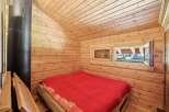 Experience cozy living in this charming wooden cabin, featuring a comfortable bed with a vibrant red blanket.