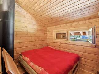 Experience cozy living in this charming wooden cabin, featuring a comfortable bed with a vibrant red blanket.