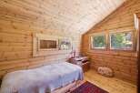 Experience cozy living in this charming wooden cabin bedroom, featuring a comfortable bed with a textured throw and a rustic red rug.