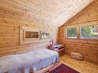 Experience cozy living in this charming wooden cabin bedroom, featuring a comfortable bed with a textured throw and a rustic red rug.