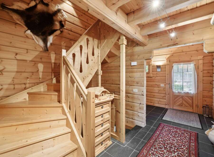 Step into a charming log cabin interior featuring a rustic wooden staircase with intricate railings and a unique animal hide mounted on the wall.