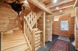 Step into a charming log cabin interior featuring a rustic wooden staircase with intricate railings and a unique animal hide mounted on the wall.