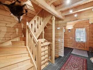 Step into a charming log cabin interior featuring a rustic wooden staircase with intricate railings and a unique animal hide mounted on the wall.