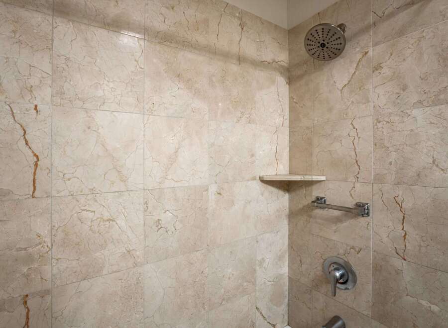 Experience luxury in this beautifully tiled shower, featuring elegant marble-patterned walls and a convenient corner shelf for your toiletries.
