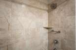 Experience luxury in this beautifully tiled shower, featuring elegant marble-patterned walls and a convenient corner shelf for your toiletries.
