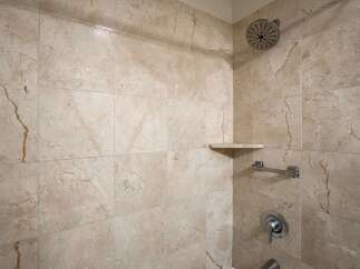 Experience luxury in this beautifully tiled shower, featuring elegant marble-patterned walls and a convenient corner shelf for your toiletries.