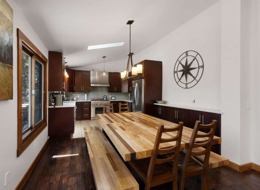 This spacious kitchen and dining area features rich, dark wood cabinetry complemented by a large, rustic butcher block dining table and benches.