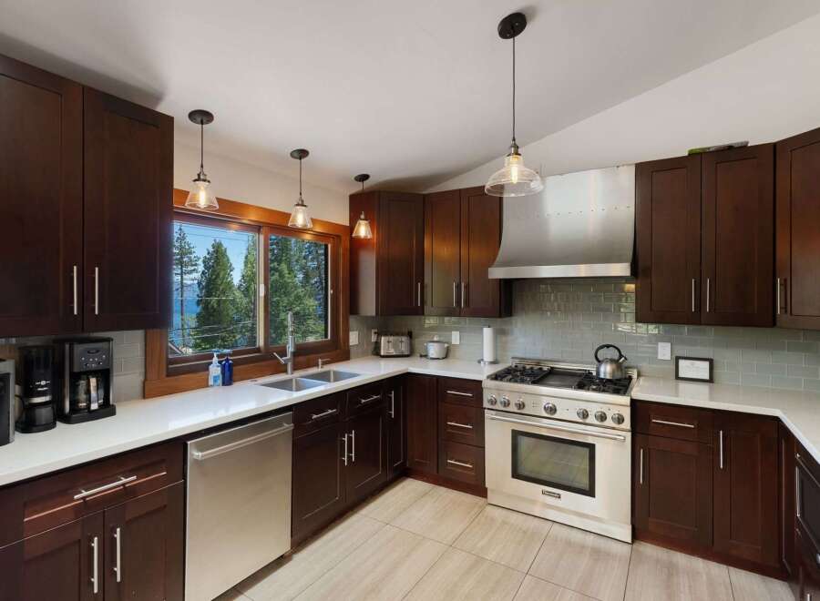 Experience breathtaking lake and forest views from this stunning kitchen, featuring rich dark wood cabinetry and sleek quartz countertops.