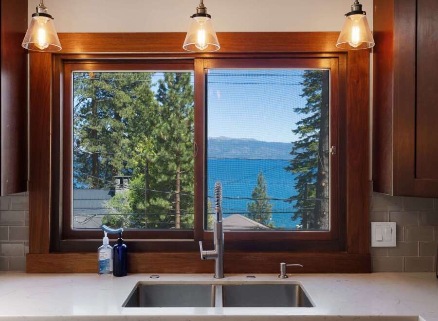 Experience breathtaking lake views from this stunning kitchen, featuring a large window overlooking the water and lush green trees.