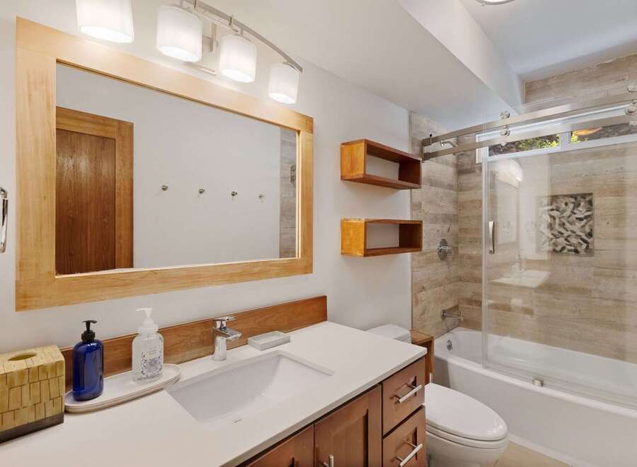 This modern bathroom features a sleek vanity with a white countertop and wooden cabinets, complemented by a large wooden-framed mirror.