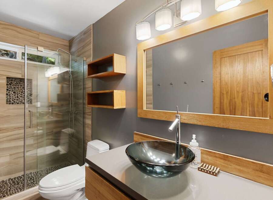 Experience modern luxury in this stunning bathroom featuring a spacious walk-in shower with natural stone accents and elegant wood-grain tile.