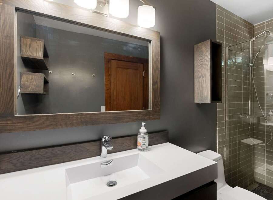 This modern bathroom features a sleek white vanity with a vessel sink and a contemporary faucet, complemented by a rustic wooden framed mirror.