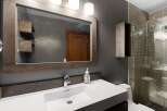 This modern bathroom features a sleek white vanity with a vessel sink and a contemporary faucet, complemented by a rustic wooden framed mirror.