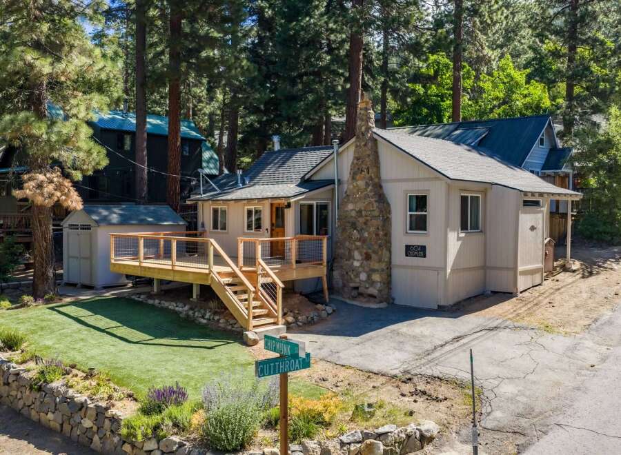 Charming cabin nestled among tall pine trees, featuring a spacious wooden deck perfect for outdoor relaxation and entertaining.