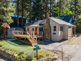 Charming cabin nestled among tall pine trees, featuring a spacious wooden deck perfect for outdoor relaxation and entertaining.