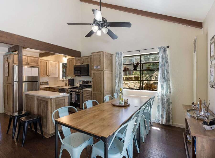 Experience rustic charm in this inviting kitchen and dining area, featuring vaulted ceilings with exposed beams and a ceiling fan for optimal comfort.
