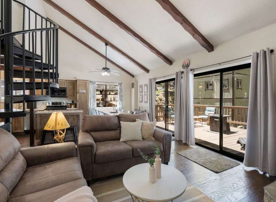 Experience cozy living in this charming cabin featuring a vaulted ceiling with exposed wooden beams and a striking spiral staircase.