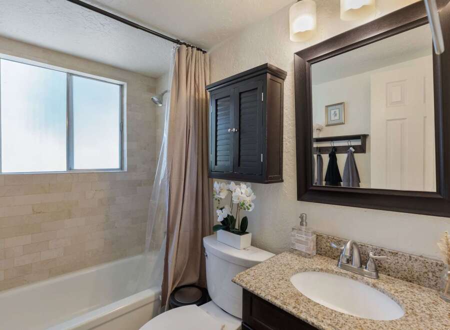 This bathroom features a bathtub with a tiled wall and a frosted window, complemented by a beige shower curtain.