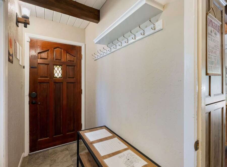 Welcome guests into this charming entryway featuring a beautiful wooden door and a convenient coat rack with a shelf for storage.