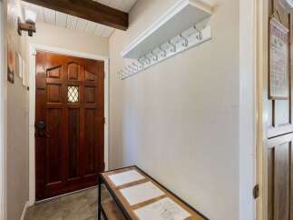 Welcome guests into this charming entryway featuring a beautiful wooden door and a convenient coat rack with a shelf for storage.