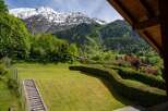 Experience breathtaking mountain views from this stunning property, featuring a lush green lawn and a charming wooden staircase leading up the hillside.