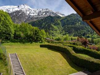 Experience breathtaking mountain views from this stunning property, featuring a lush green lawn and a charming wooden staircase leading up the hillside.