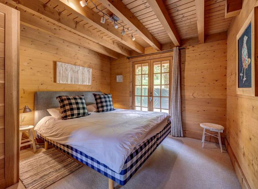 Experience rustic charm in this cozy bedroom, featuring warm wood paneling throughout and exposed ceiling beams.