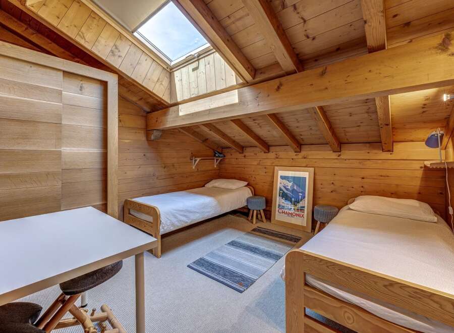 Experience cozy mountain living in this charming attic bedroom, featuring two comfortable twin beds and a dedicated workspace.