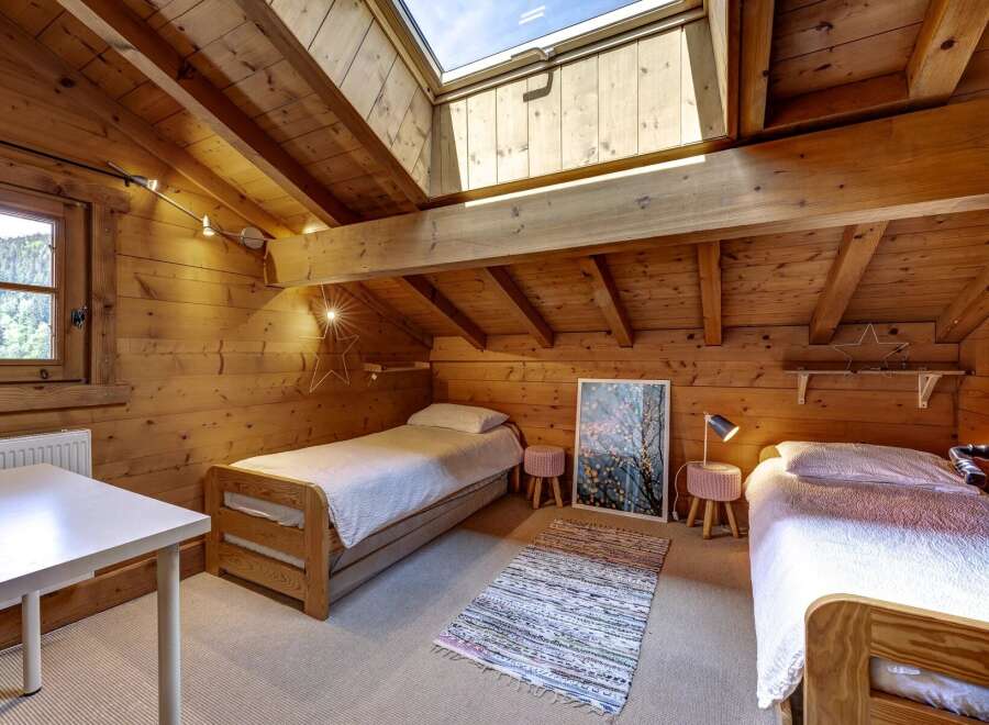 Experience cozy living in this charming attic bedroom, featuring warm wooden walls and a vaulted ceiling with a skylight that floods the space with natural light.