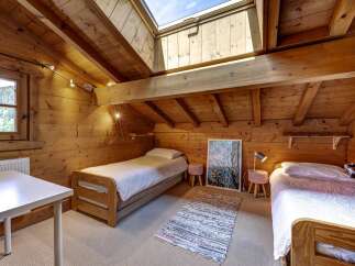 Experience cozy living in this charming attic bedroom, featuring warm wooden walls and a vaulted ceiling with a skylight that floods the space with natural light.