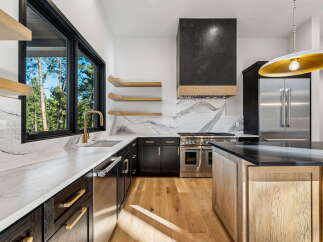Experience luxury in this modern kitchen featuring dark wood cabinetry, sleek marble countertops, and a striking black range hood.