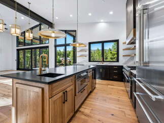 Experience luxury mountain living in this stunning modern kitchen, featuring a large island with a waterfall countertop and a sleek brass faucet.