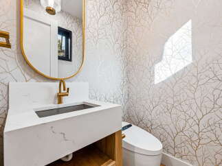 This modern bathroom features a striking gold-framed oval mirror above a sleek white vanity with a marble countertop and a gold faucet.