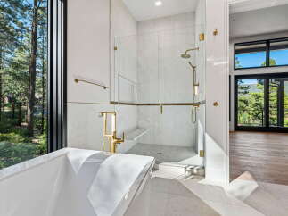 Experience luxury in this stunning bathroom featuring a freestanding soaking tub and a spacious glass-enclosed shower with elegant gold fixtures.