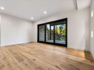 Experience modern living in this spacious room featuring elegant hardwood floors and a wall of glass sliding doors that open to a stone patio and lush greenery.