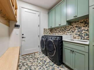 This laundry room boasts a stylish pebble tile backsplash and coordinating sage green cabinetry, creating a serene and functional space.