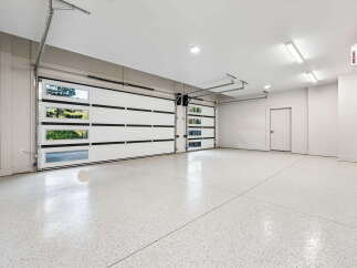 This spacious garage features two modern, white sectional garage doors with clear glass panels, allowing natural light to illuminate the interior.