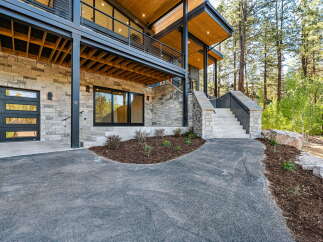 Experience modern mountain living in this stunning home featuring a sleek garage door and expansive windows that invite the natural beauty of the surrounding pine forest indoors.