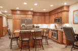 This spacious kitchen features warm oak cabinetry, a large stainless steel refrigerator, and a granite-topped island with bar seating.