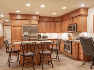 This spacious kitchen features warm oak cabinetry, a large stainless steel refrigerator, and a granite-topped island with bar seating.