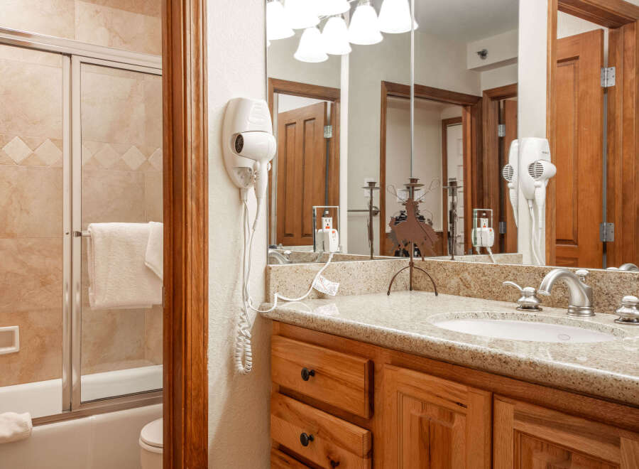 This charming bathroom features a spacious bathtub with a sliding glass door and a convenient wall-mounted hairdryer.