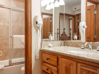 This charming bathroom features a spacious bathtub with a sliding glass door and a convenient wall-mounted hairdryer.