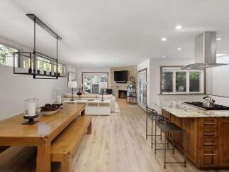 Experience open-concept living in this beautifully appointed home, featuring a spacious dining area with a modern chandelier and a cozy living room with a stone fireplace.