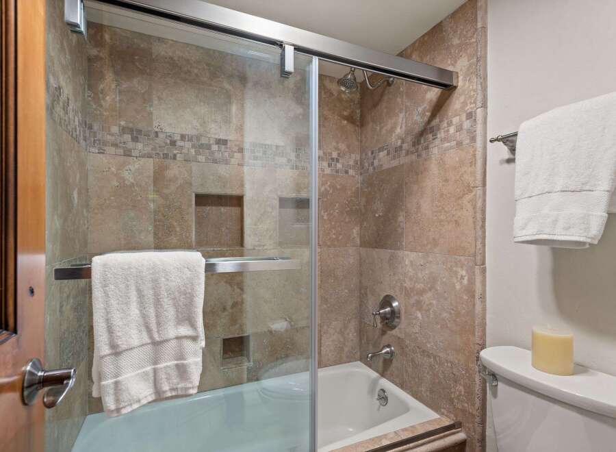 Experience luxury in this bathroom featuring a spacious bathtub with a glass enclosure and elegant travertine tilework.