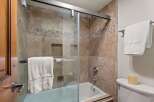 Experience luxury in this bathroom featuring a spacious bathtub with a glass enclosure and elegant travertine tilework.