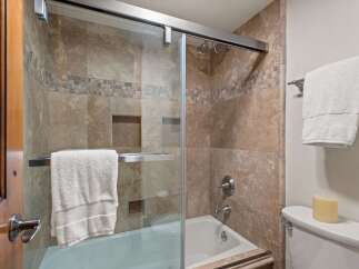 Experience luxury in this bathroom featuring a spacious bathtub with a glass enclosure and elegant travertine tilework.