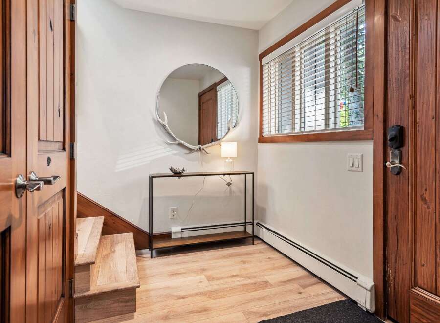 Step into this inviting entryway featuring warm wooden doors and stairs, complemented by a stylish console table with a unique antler-adorned mirror.